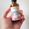 Una mano sosteniendo una bruma aromática con etiqueta con flores y perlas