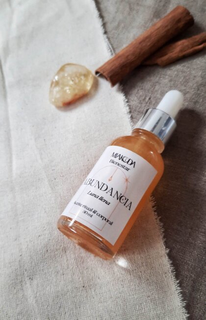 Frasco gotero de aceite aromático dorado, junto a un cuarzo cristal y canela en rama para la abundancia