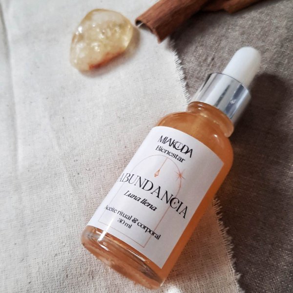 Frasco gotero de aceite aromático dorado, junto a un cuarzo cristal y canela en rama para la abundancia