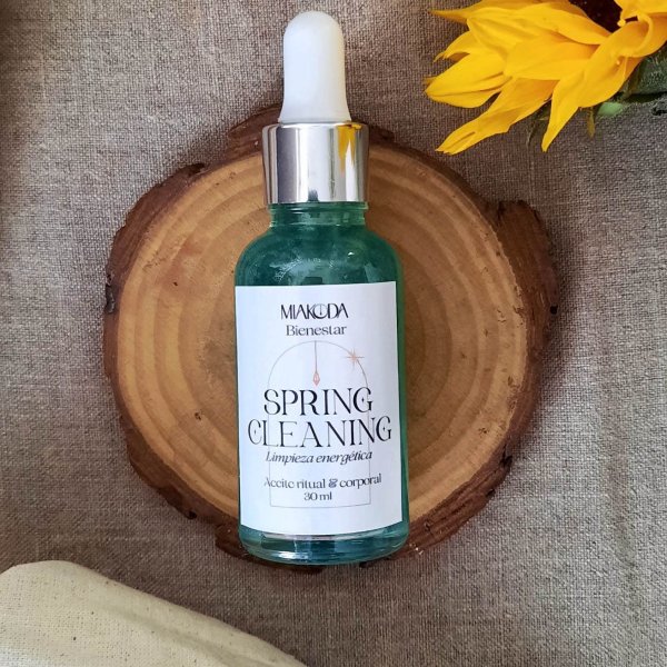 Frasco gotero de aceite color turquesa con etiqueta blanca, junto a una flor amarilla