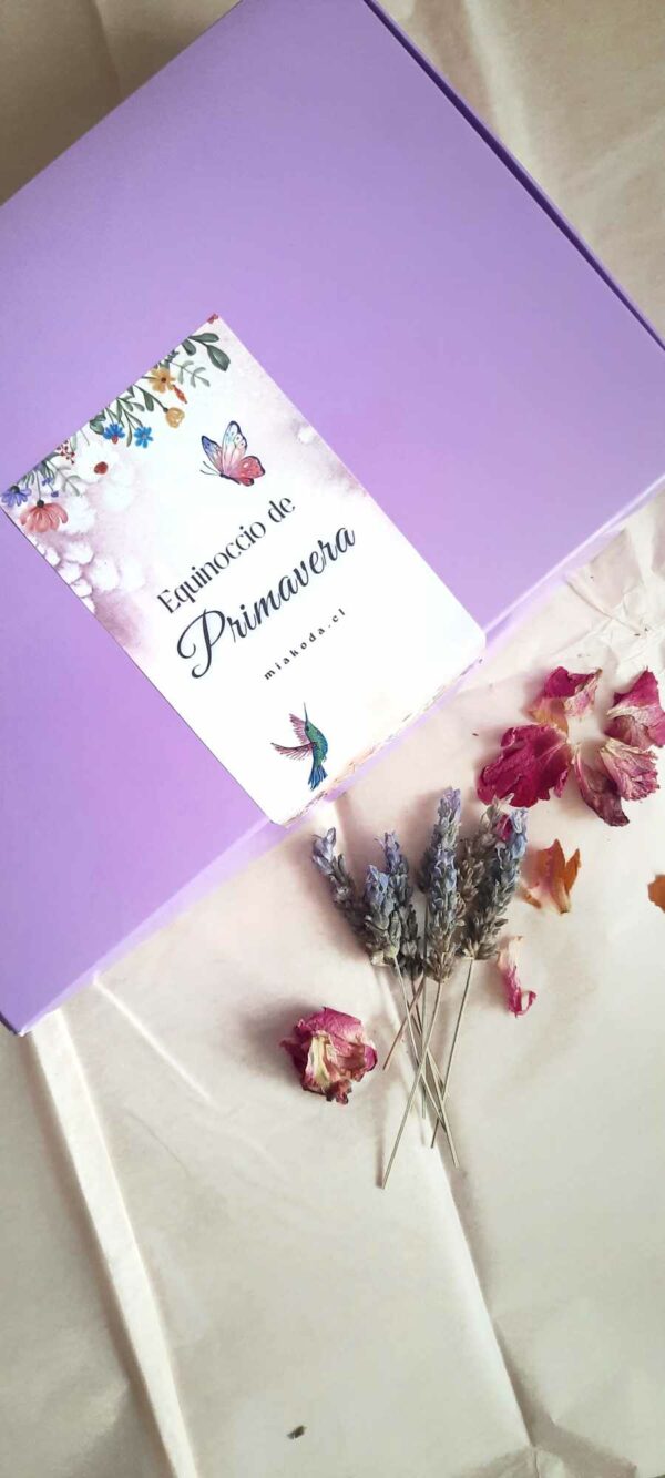 Caja color lila con etiqueta blanca y rosas y lavandas junto a ella