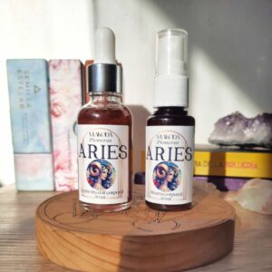 Set de frascos, uno de spray otro de aceite de aromas, del signo Aries. Ambos están delante de un ambiente místico, con cristales y oráculos