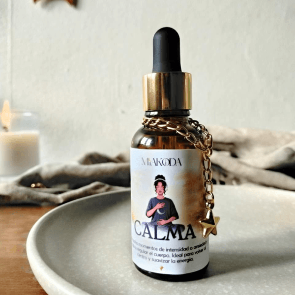 Frasco de aceite esencial Miakoda 'CALMA' con etiqueta ilustrada, junto a una vela y elementos de bienestar diario.