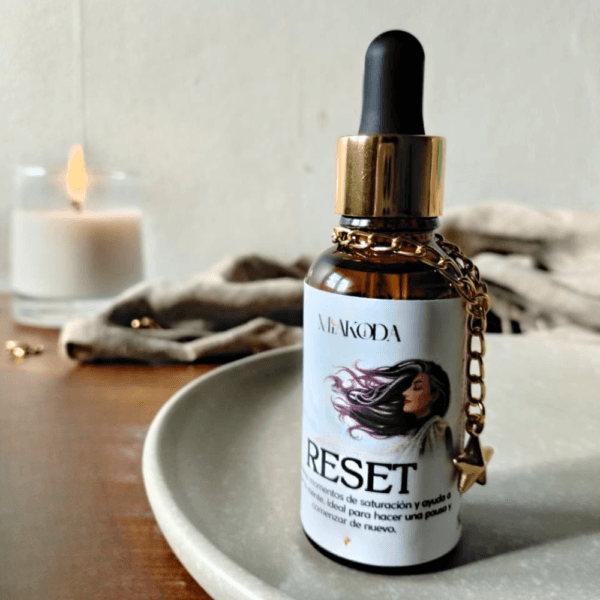 Aceite esencial Miakoda 'RESET' en frasco con cuentagotas y amuleto, sobre mesa de madera, ideal para rituales de bienestar.