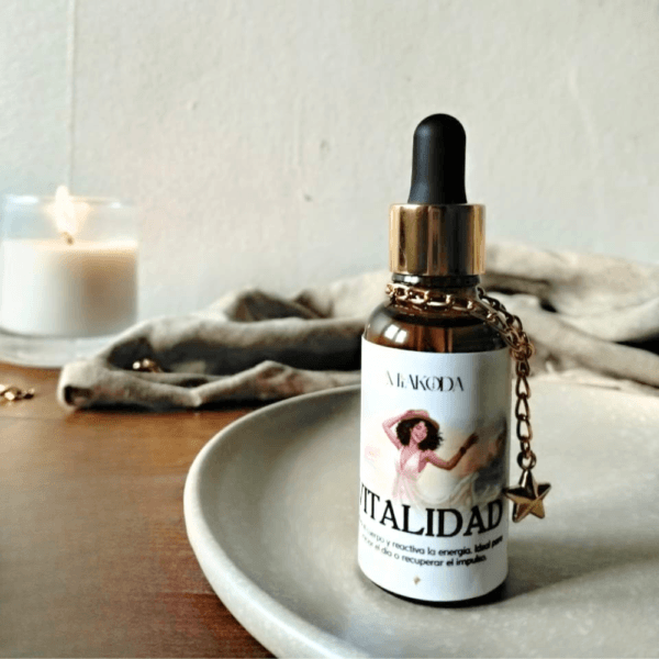 Frasco de aceite esencial Miakoda 'VITALIDAD' con etiqueta ilustrada, sobre plato de cerámica y vela encendida, estilo místico.