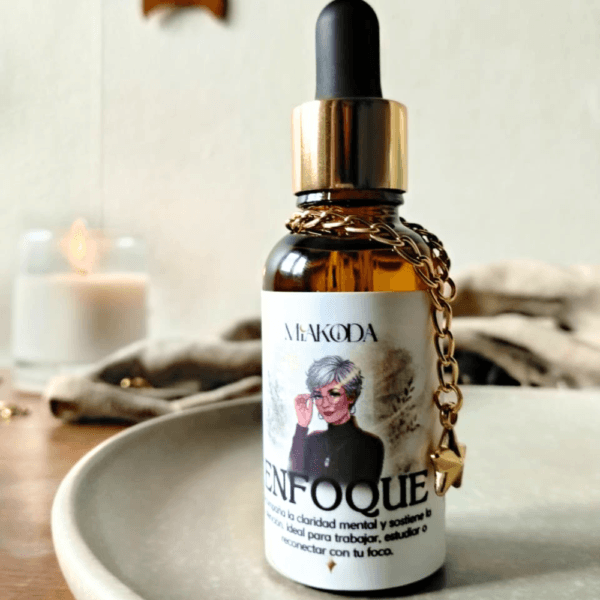 Frasco de aceite esencial 'ENFOQUE' Miakoda con cuentagotas y amuleto dorado, junto a una vela, ideal para claridad mental.